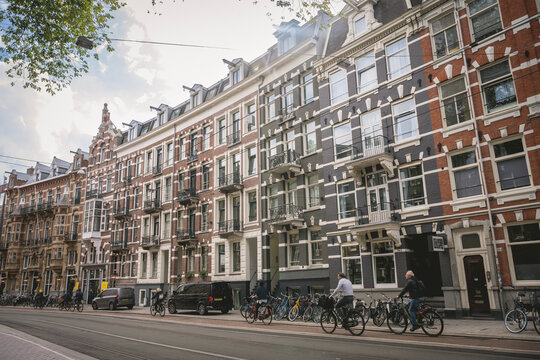 Historic European street with bicycles, lined with brick townhouses under a partly cloudy sky. Amsterdam,. Netherlands