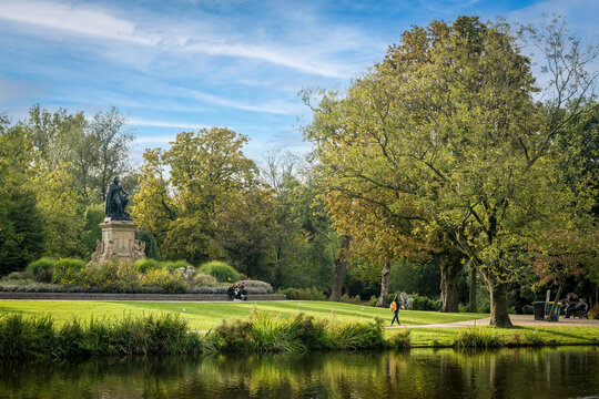 A serene park landscape with a statue, walking paths, and a reflective pond under a blue sky. Amsterdam,. Netherlands
