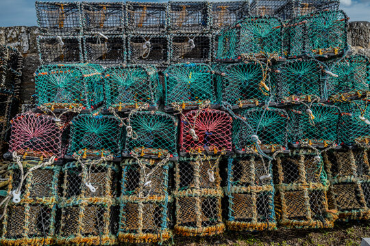 Stacked multicolored lobster traps with nets piled against a stone wall. Keiss harbour, Scotland