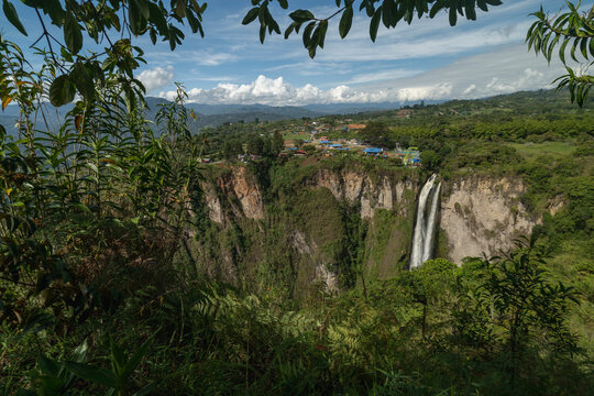 Majestic waterfall cascades down a lush, green cliff with a village in the background. San Agustin, Colombia