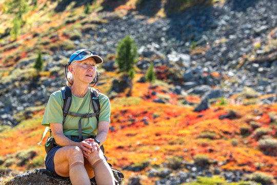 Woman in hiking gear rests on a rock amidst colorful autumn mountain landscape. Valle d'Aosta, Italy