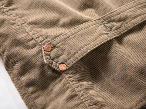 Close-up of brown denim fabric with copper button details and visible stitching.
