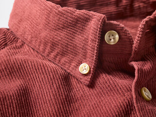 Close-up of a red corduroy shirt with beige buttons on a white background.