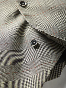 Close-up of a plaid fabric with black buttons and detailed stitching.