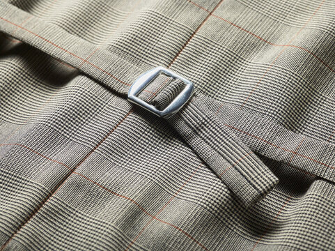Close-up of a fabric belt with a metal buckle on plaid textile.