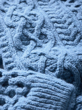 Close-up of a blue knitted wool sweater with intricate cable patterns.