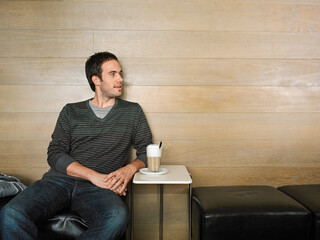 Young man sitting on a sofa with a coffee cup on a small table in a minimalist setting. Germany