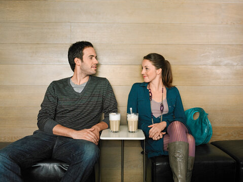 A man and woman sit together on a cafe bench, sharing drinks and engaged in conversation.   Germany