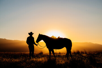 Cowboy and horse silhouetted by a glowing sunset in a grassy landscape. Oregon, USA