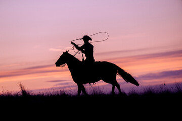 Silhouette of a cowboy on horseback twirling a lasso at sunset. Oregon, USA