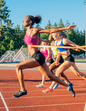 Female athletes sprint across the finish line on a sunny outdoor track in vibrant sportswear. WA, USA