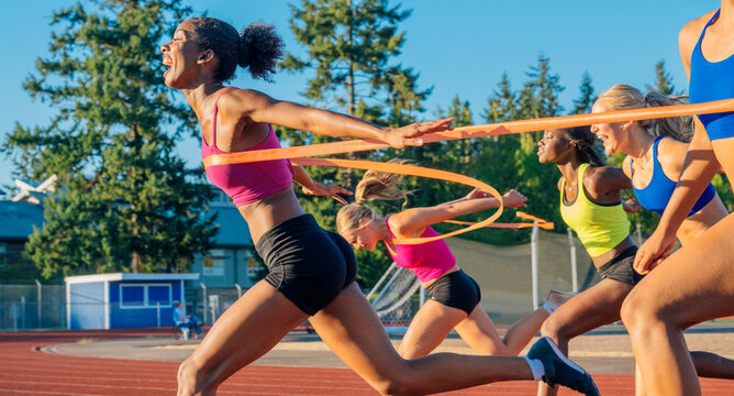 Women sprint across a finish line on a sunny outdoor track, celebrating their achievement. WA, USA
