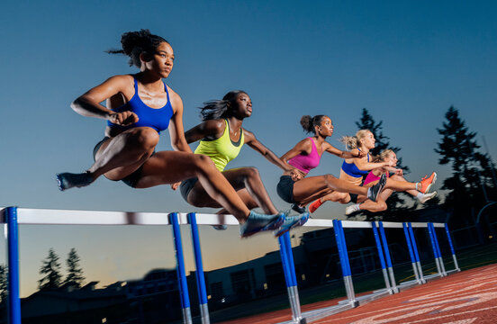 Group of athletes jumping over hurdles on a running track at sunset in vibrant sportswear. WA, USA