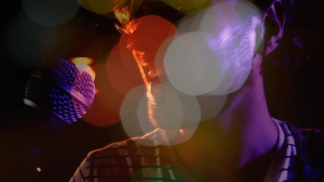 Male singer opening mouth and singing into mic during music set, colored bokeh obscuring face