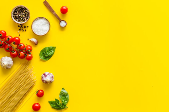 Flat lay of uncooked spaghetti with ingredients for cooking Italian pasta - tomatoes and basil with garlic - on a yellow background, top view