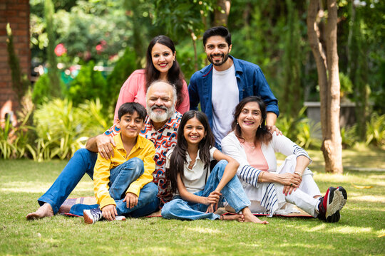 Indian family of three generations smiling and bonding outdoors on green park lawns - Powered by Adobe