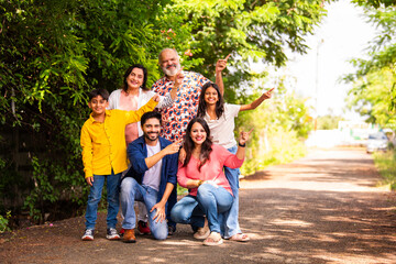 Fototapeta premium Happy Indian family of six sitting on lawn and pointing to present something outdoors.