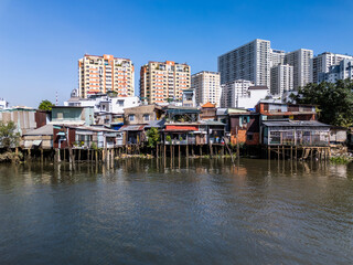 Waterfront slum houses along Kenh Te canal in Saigon or Ho Chi Minh City, Vietnam.High-rise development dominates background in district four on a sunny day .