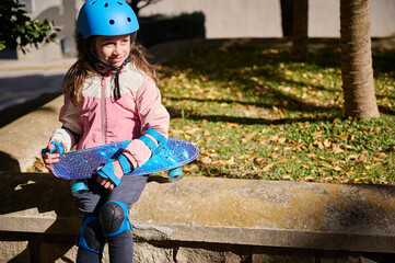 Little Girl In Blue Helmet Holding Skateboard Outdoors On Sunny Day