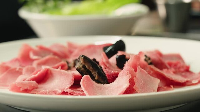 Delicious Spanish or italian ham served as rolls with green olives on white plate, chef cooking buffet menu. 