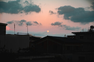 Full moon over city rooftops silhouettes at night sky