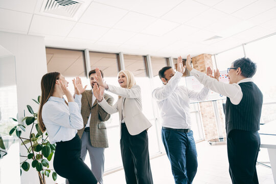 Group of business professionals celebrating teamwork success in a modern office space with vibrant energy - Powered by Adobe
