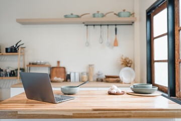 Modern laptop on wooden kitchen island with bowls, plate and utensils evoking cozy productivity and home cooking