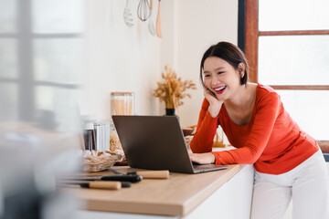 Young woman smiling while using laptop in bright kitchen, happy casual lifestyle scene