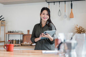 Young woman holding tablet smiling in modern kitchen with utensils and spices