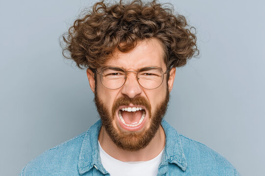 Angry young adult man with curly hair and glasses expressing frustration