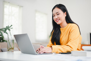 Obraz premium Young woman laptop remote work at home smiling in bright living room, relaxed and focused on screen