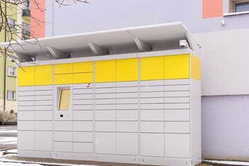 Parcel locker in winter. Yellow parcel locker stands beside residential building in snowy weather. Concept of delivery infrastructure, urban logistics, e-commerce visual, and modern city service.