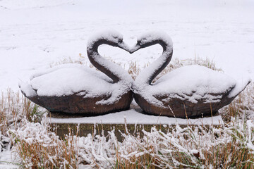 Snow on swan sculptures. Pair of swan sculptures covered with snow on grass. Concept of winter romance, symbolic love theme, and decorative garden imagery.