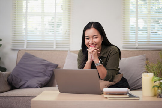 Young woman smiling during video call on laptop in cozy living room with pillows and plants