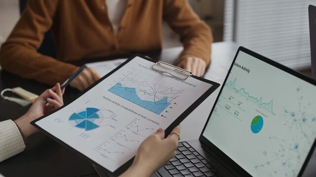 Cropped shot of businesspeople analyzing financial charts on documents and laptop while meeting at office desk