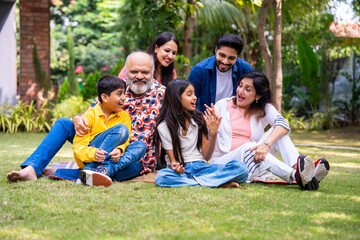 Indian family of three generations smiling and bonding outdoors on green park lawns