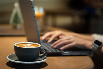 Close-up of Hot coffee latte with latte art milk foam in cup mug and laptop computer on wood desk office desk in coffee shop at the cafe,during business work concept