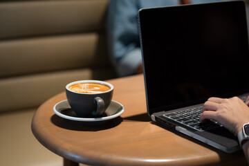 Close-up of Hot coffee latte with latte art milk foam in cup mug and laptop computer on wood desk office desk in coffee shop at the cafe,during business work concept
