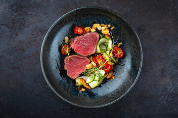 Fine dry aged beef filet steak rare tataki style cut tagliata with sliced zucchini, tomato and almonds served as top view in a design bowl