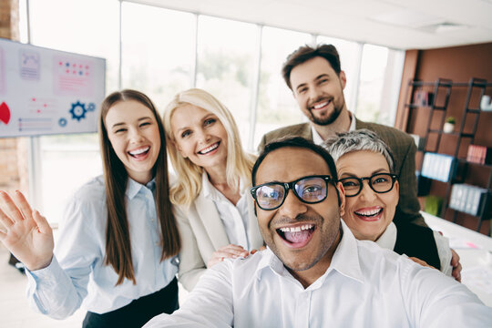 Group of cheerful colleagues taking a selfie together in a modern office environment with teamwork and collaboration vibes
