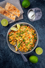 Couscous salad with chickpeas, green beans, carrots, green peas, flatbread and yogurt served as top view in a design bowl