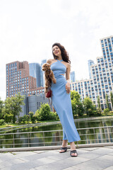Fototapeta premium Young beautiful brunette woman in blue knitted dress posing in summer park