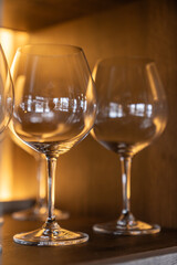 Close-up of clean empty wine glasses on a wooden shelf with warm ambient lighting in an upscale restaurant interior.