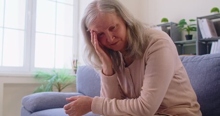 Sad, upset, worried, stressed senior woman sitting on sofa at home thinking about problems. Old woman going through hard times, experiencing difficult financial situation, feeling anxious and nervous