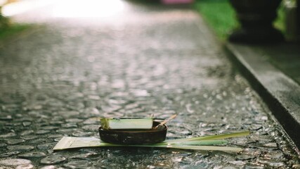 Balinese Canang Sari offering placed on a stone pathway with morning incense smoke