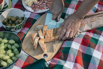 Hands of an unrecognizable person slicing baguette for a family picnic outdoors