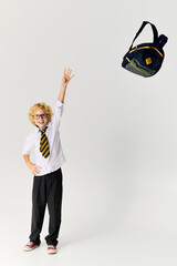 Excited schoolboy with wavy hair tosses backpack in a bright studio setting