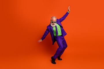 Elderly man in bright purple suit dances against orange backdrop promoting retro style and festive...