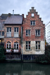 Two charming medieval buildings stand side by side on the banks of the River Lys in Ghent, Belgium. Their rustic red brick fa&ccedil;ades and simple windows overlook the canal