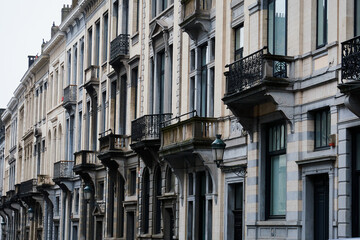 Elegant row of traditional residential buildings with detailed balconies and arched windows in Brussels, Belgium. Captured on a cloudy day, the image highlights the architectural charm
